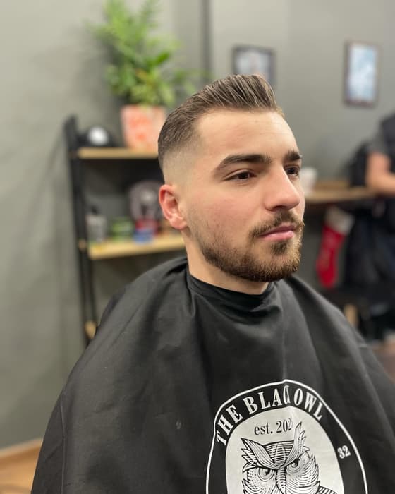 Quiff με fade και γένια, με τη μαύρη κάπα του μαγαζιού