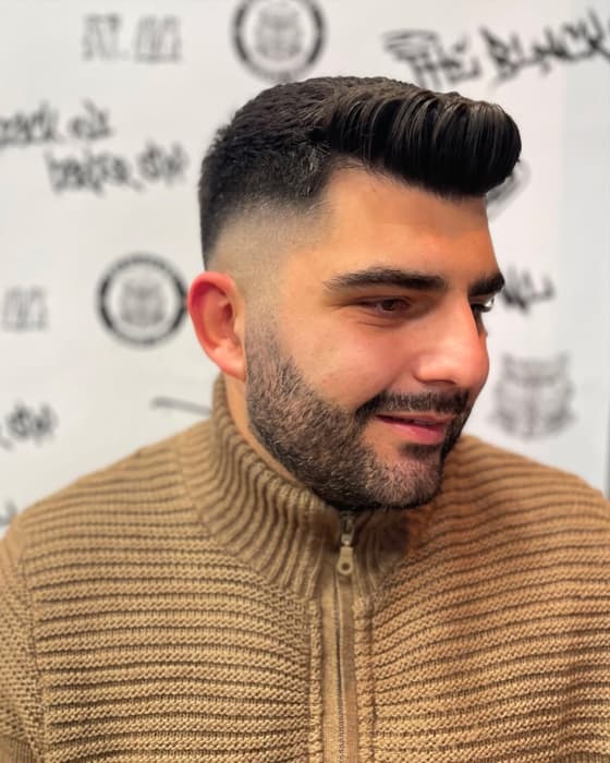Pompadour με fade και γένια, μπροστά στον τοίχο του μαγαζιού